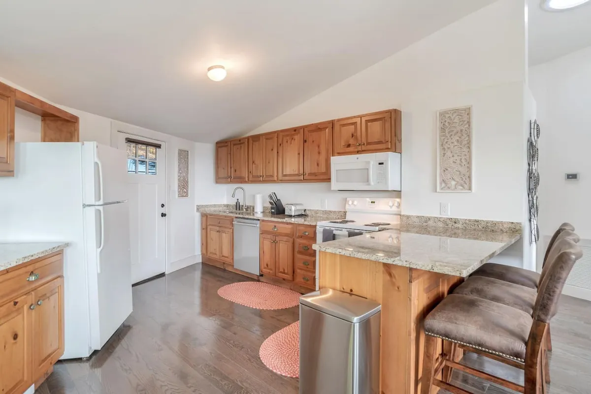 The kitchen features granite countertops, wooden cabinetry, bar stools, and modern appliances. The layout invites casual family meals or snack prep before heading out to hike, echoing the family-centric and adventure-ready feel of the cottage.