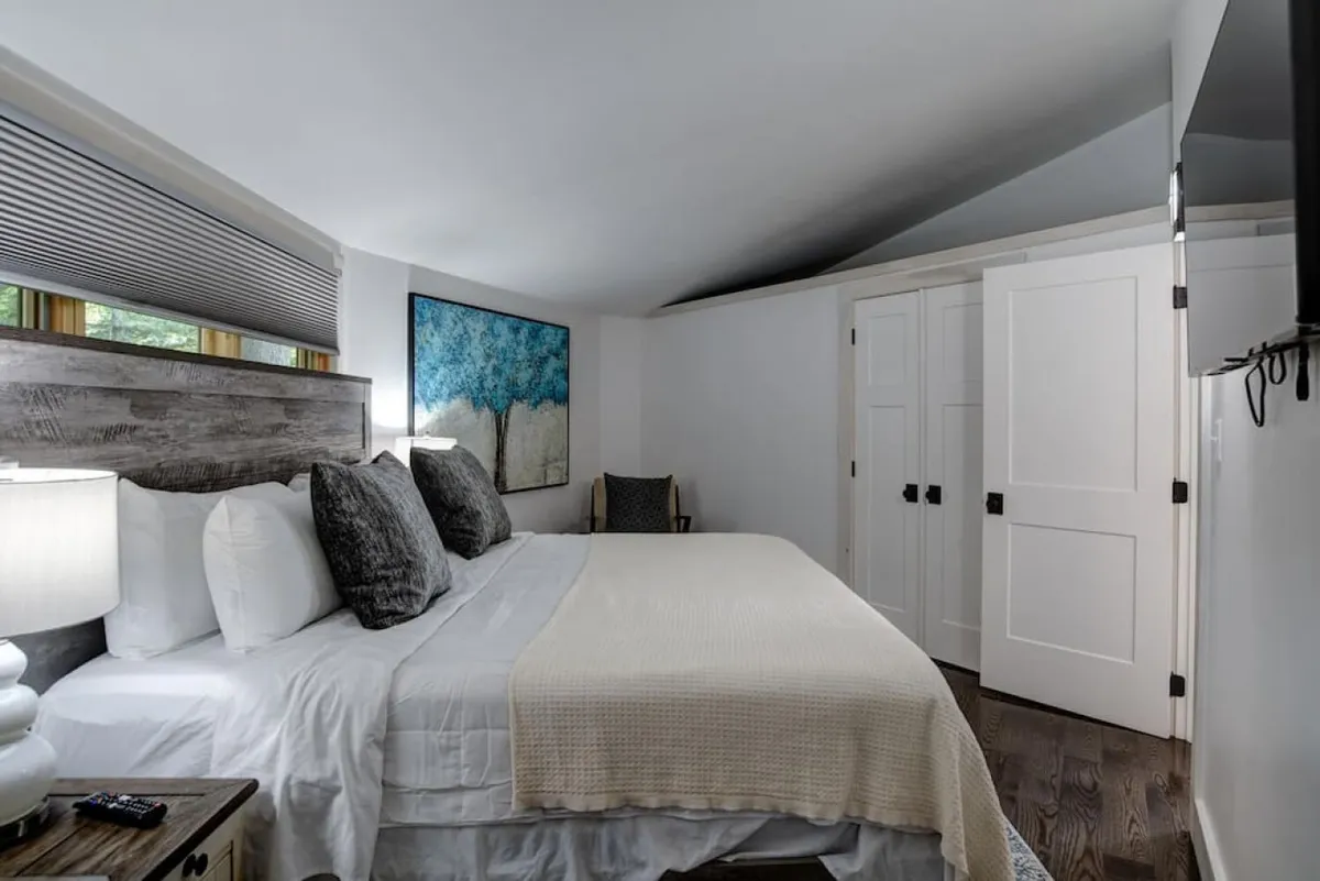 A king-size bed dressed in luxury bedding sits at the center of the room, accented by textured throw blankets and soft lighting from a bedside lamp. Artwork on the wall and calming décor create a restful, inviting atmosphere ideal for unwinding after a day of mountain adventures.