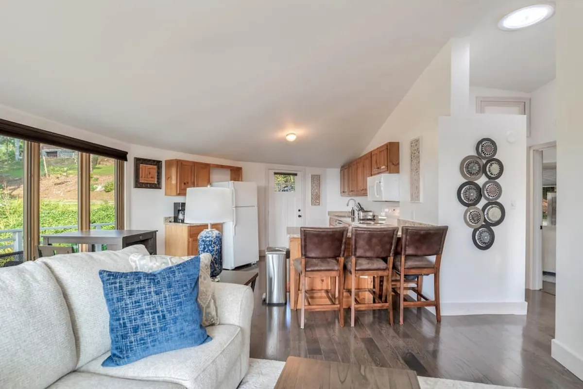 An open-concept interior that combines a sofa, dining table, kitchen area, and expansive windows. The layout fosters easy interaction, making it ideal for families or groups to gather, dine, and unwind in a sunlit, welcoming setting.